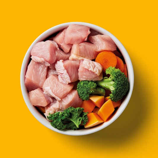 Bowl of Raw Turkey 1kg with broccoli, carrots, and kale on a vibrant yellow background.