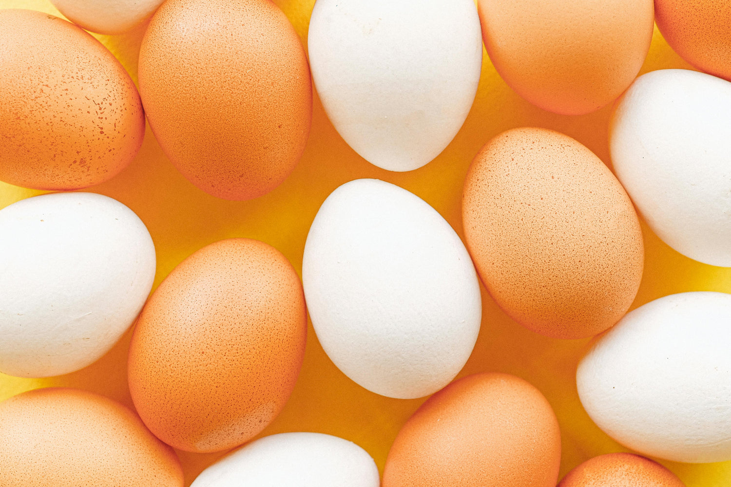 Brown and white eggs arranged closely together on a yellow background.