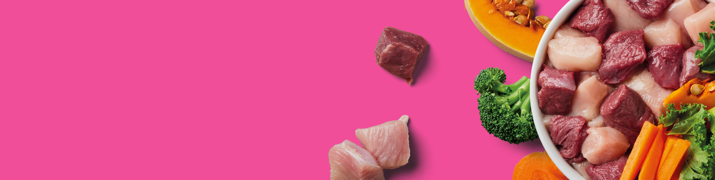 A bowl filled with raw meat cubes, broccoli, carrot sticks, and pumpkin sits on a pink background, with a few pieces of raw meat and vegetables scattered nearby.