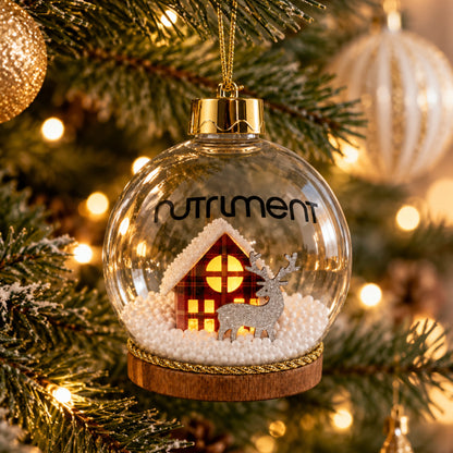 A Light-Up Christmas Bauble 1pc made of clear glass with a miniature cabin and reindeer hanging on a tree.