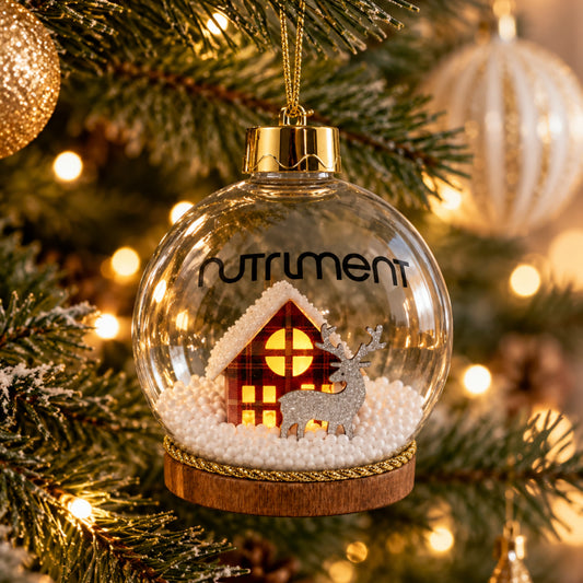 A Light-Up Christmas Bauble 1pc made of clear glass with a miniature cabin and reindeer hanging on a tree.
