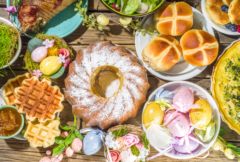 Easter brunch spread with waffles, bread rolls, bundt cake, quiche, salad, and decorated Easter eggs.