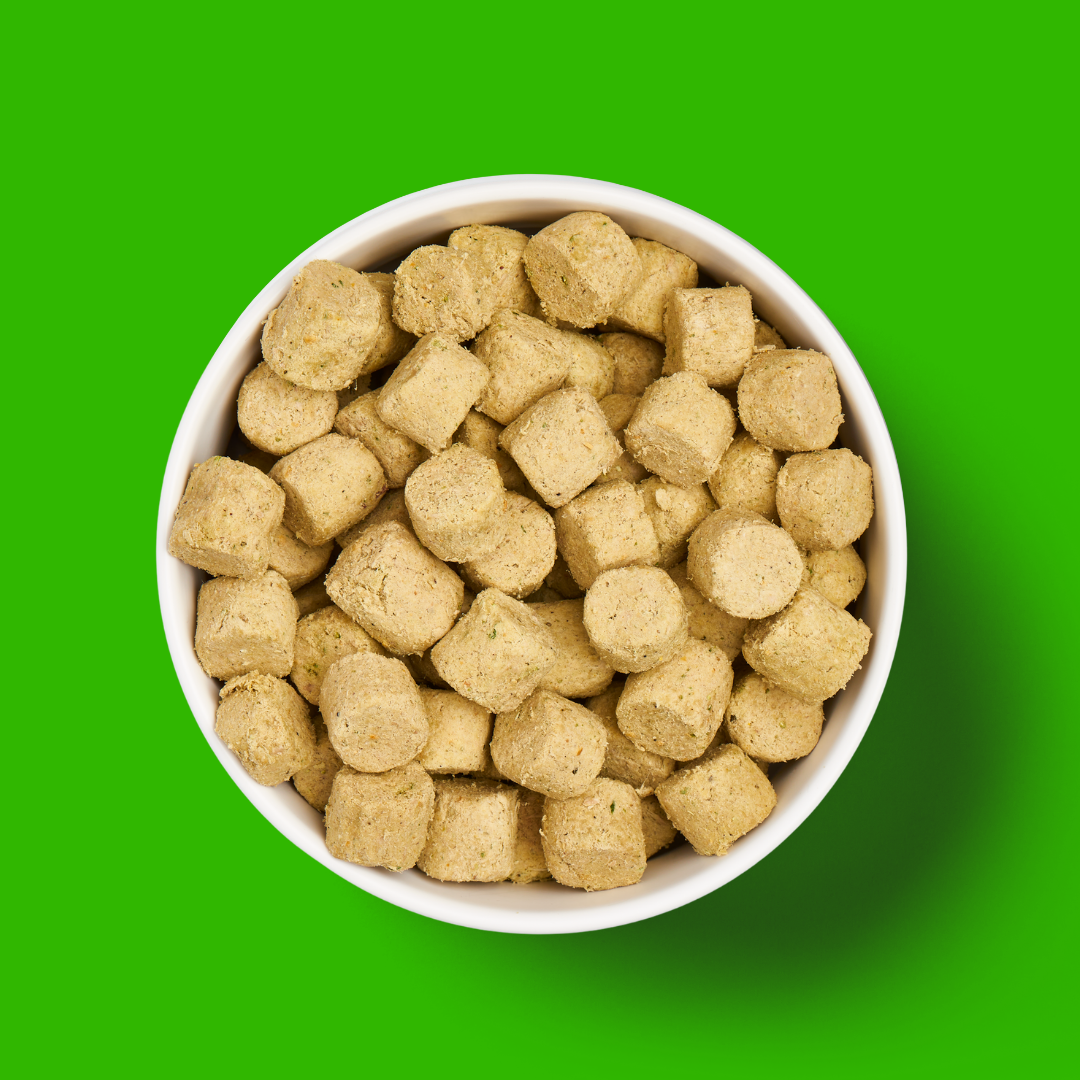 A white bowl of Freeze Dried Food - Lamb 225g pellets on a bright green background.