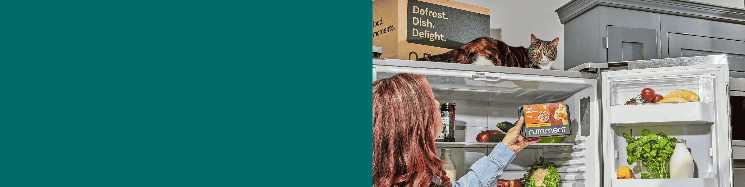 A person holds a frozen meal near an open fridge full of vegetables; a cat sits on the fridge.