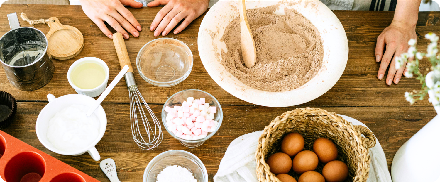 Two people preparing to bake with bowls of ingredients, eggs, and utensils arranged on a wooden table.
